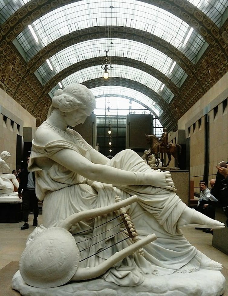 Estatua de una mujer con las piernas cruzadas mirando al suelo.